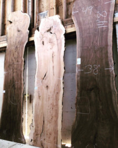 3 long slabs of live edge wood leaning against a warehouse wall